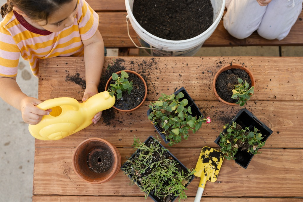 Child watering plants at potting table